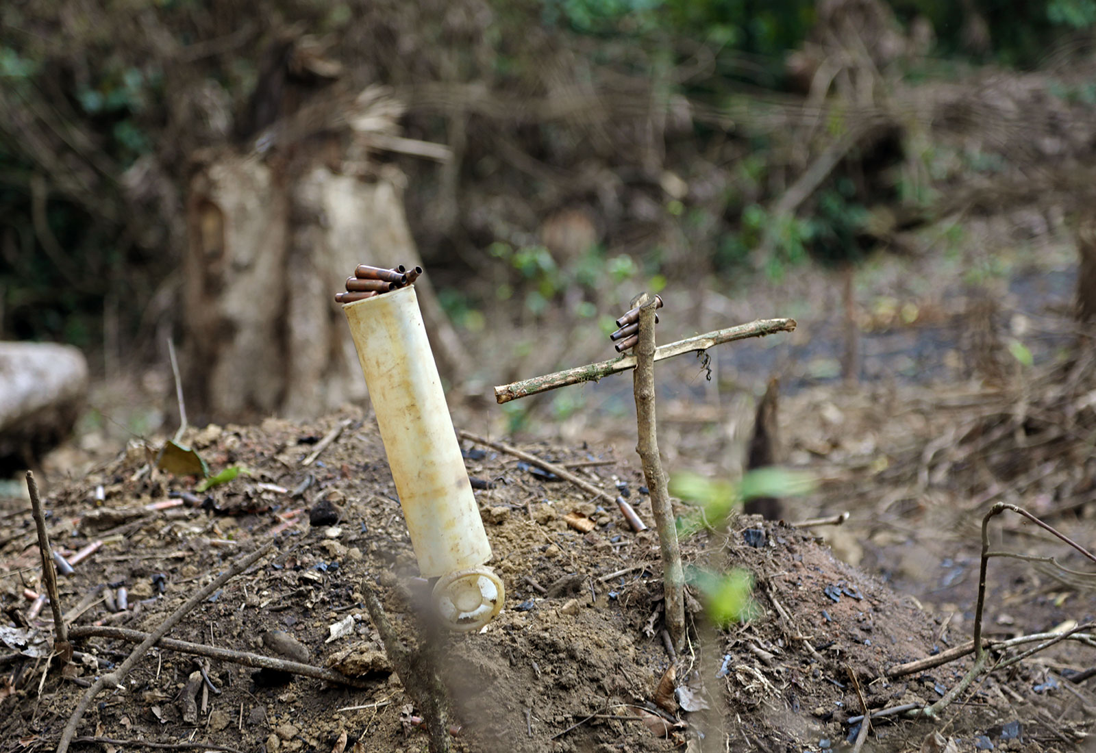 A pile of dirt with a plastic pipe and a cross made of branches with bullet casings