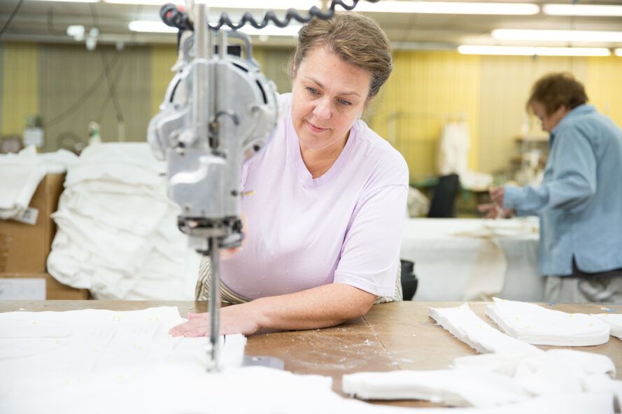 A woman in a light pink shirt sews together white fabric