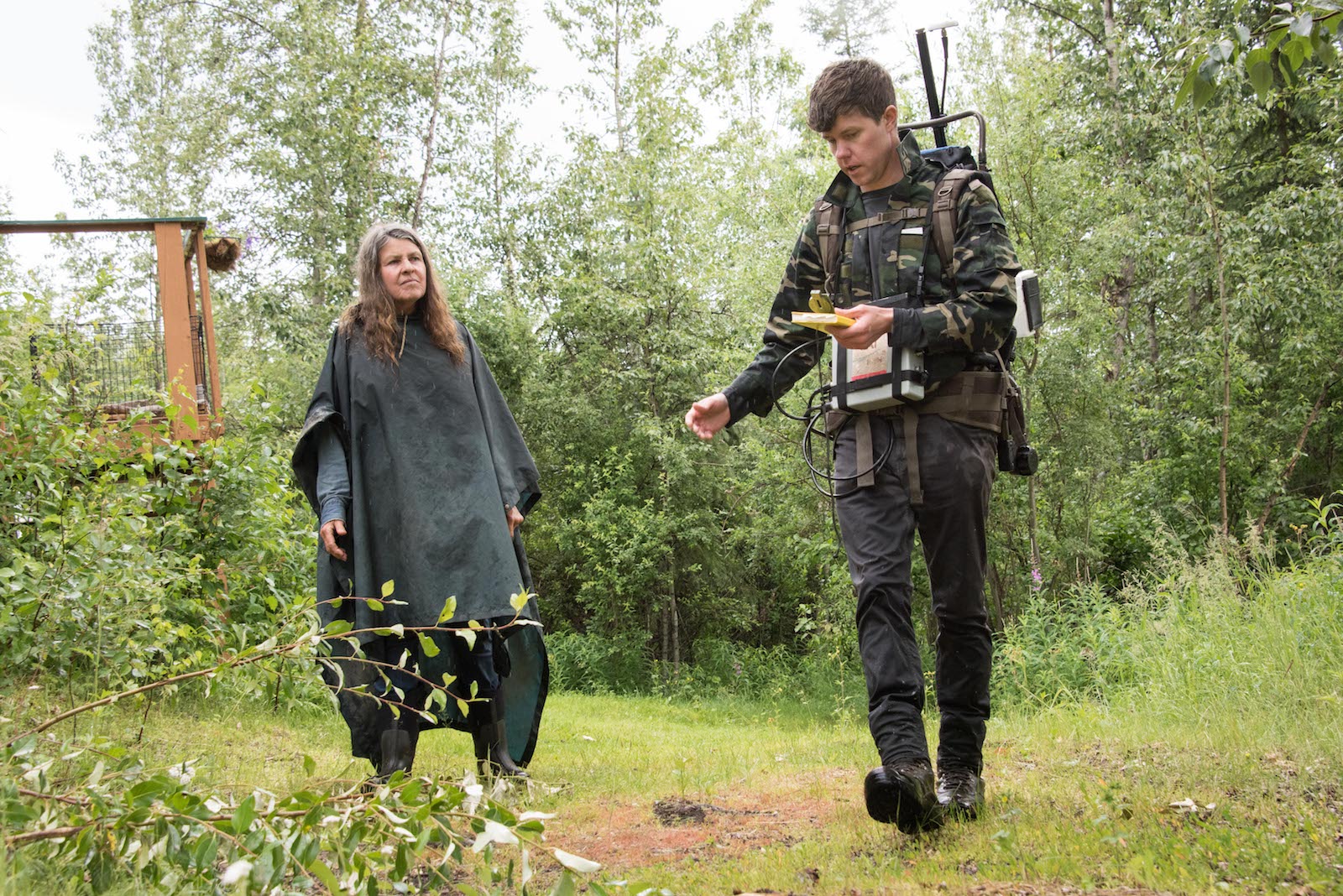 a man in green nature clothes and a woman in a poncho walk in a forest