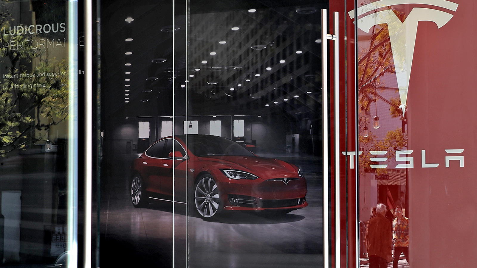 Tesla showroom viewed from outside; red car and banner with Tesla logo visible through window